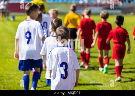 Los jugadores de fútbol para niños entrando en tono después de árbitro en dos filas. Equipos de fútbol juvenil torneo partida coinciden. Los muchachos en rojo y blanco jerse fútbol