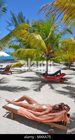 Frau Junge sonnt sich unter Palmen am Meer | joven sol bajo palmeras en una tumbona en una playa de arena Foto de stock