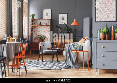 Luz naranja sobre beige sofá en gris espacio abierto interior con un sillón y una silla en la mesa de comedor Foto de stock
