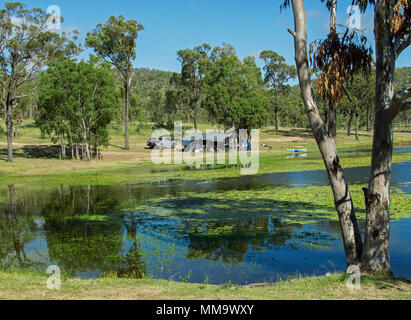 Los campistas con carpa y coche en el impresionante paisaje boscoso que se refleja en tranquilas aguas azules del lago bajo un cielo azul en la represa Eungalla Australia Foto de stock