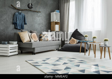 Nuevo apartamento interior en gris con sofá, moderno puf, una pequeña mesa, dos sillas y una alfombra de patrón