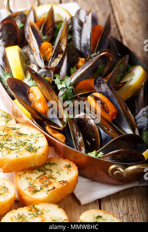 Francés de mariscos mejillones con limón, perejil y ajo de cerca en una olla de cobre y tostadas en la tabla vertical, estilo rústico.