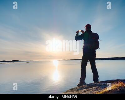 Silueta de hombre conservar recuerdos con la cámara del teléfono en su mano. Maravillosa puesta de sol en el mar, buen nivel de agua