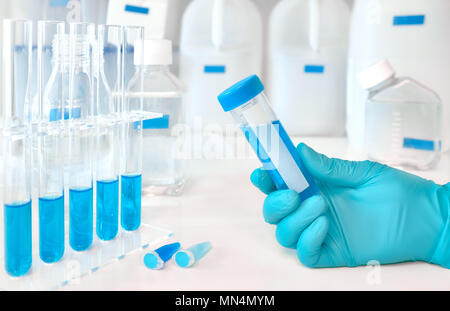 Antecedentes científicos, en azul y blanco. Muestra de líquido en el lado femenino enguantada, azul muestras líquidas en tubos de vidrio y plástico Foto de stock