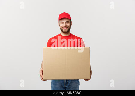 Entrega logística sonriente joven hombre en uniforme rojo sosteniendo el cuadro sobre fondo blanco.