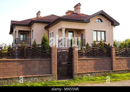 Moderna casa lujosa de dos pisos con techo de tejas negras, paredes  blancas, porche, jardín con césped, arbustos florecientes, palmeras  Fotografía de stock - Alamy