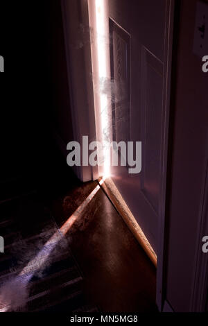 Luz brillante y emisión de humo a través de una puerta ligeramente abierta dentro de una casa.