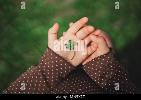 Trébol de cuatro hojas verdes en las manos del niño pequeño de feliz joven niña.