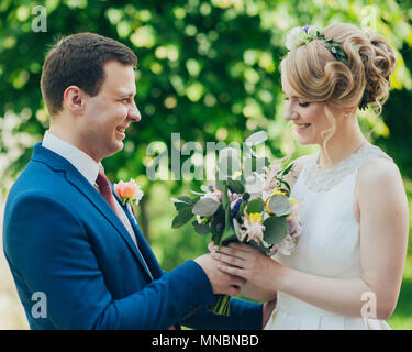 Feliz sonriente elegante para el novio y la novia en el verano parque verde con bouquet de flores, bailando y divirtiéndose en el día de su boda Foto de stock