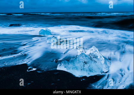 Rocas de hielo próximas bañadas por las olas del océano Atlántico, en la arena negra de origen volcánico en el diamante beach, Islandia abril 2018