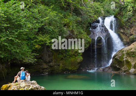 Padre e hijo están sentados en una roca y mirar la famosa cascada Sum en Vintgar Gorge, Eslovenia. La Vintgar Gorge es un barranco en la inmediata v Foto de stock