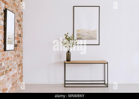 Póster de pared simple en blanco encima de la mesa con planta en jarrón negro en galería de arte Foto de stock