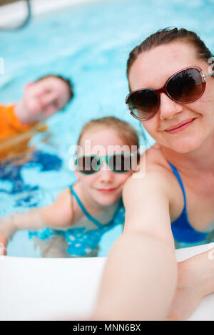Feliz madre de familia y sus hijos en la piscina tomando selfie en vacaciones tropicales
