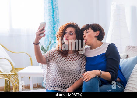 Dos jóvenes mujeres tomar fotografías con el teléfono móvil en casa haciendo lindo y divertido expresiones. mejores amigos que aman a comunicarse en la red con frie