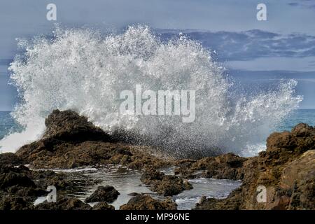 Las olas rompen en las rocas en Mermaid Tutukaka piscinas en la costa, al norte de Nueva Zelanda. Las mareas y el tiempo son clave para presenciar este espectáculo mágico Foto de stock