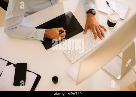 Vista superior de un hombre escrito el digitalizador con un ordenador delante. Hombre trabajando en un equipo con una taza de café en la mesa.