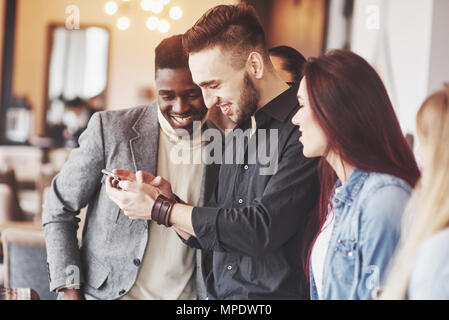 Retrato de alegres jóvenes amigos mirando teléfono inteligente mientras está sentado en la cafetería. Personas de raza mixta en un restaurante a través de teléfono móvil