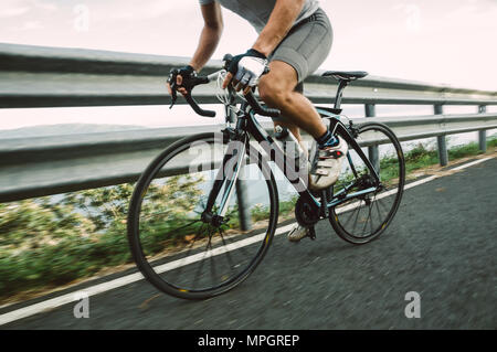 Detalle de una bicicleta de carretera con un ciclista pedaleando en una carretera.