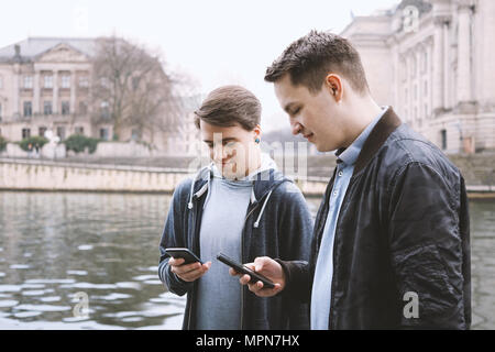 Dos teléfonos móviles antisociales adictos varones adolescentes juntos utilizando la tecnología smartphone, concepto, ubicación ribereña urbano de Berlín en Alemania Foto de stock