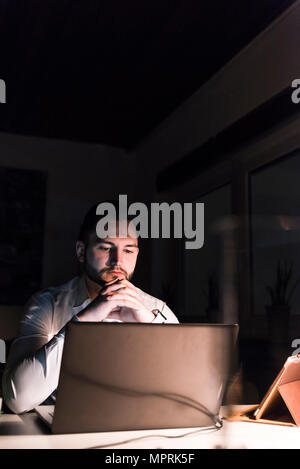 Retrato del empresario sentados frente al escritorio en la oficina por la noche mirando portátil