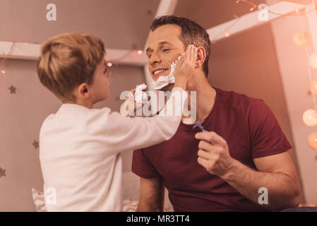 Encantado agradable muchacho ayudando a su padre a afeitarse Foto de stock