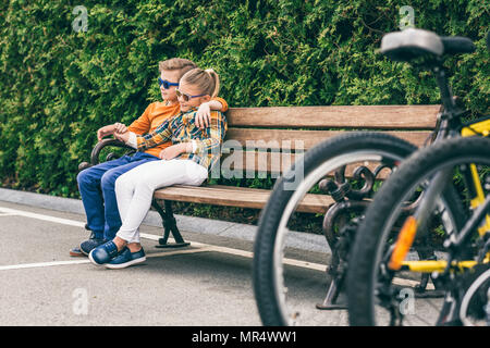 Niñito abrazando chica mientras descansa junto en un banco en el parque Foto de stock