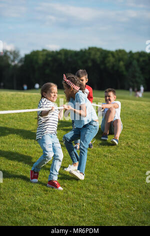 Grupo multiétnico de niños jugando Tug of war en la pasto verde en park