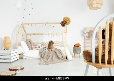 Chica leyendo un libro sobre su cama en el dormitorio moderno blanco y beige Foto de stock
