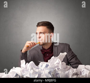 Empresario joven sentada detrás de papel arrugado con fondo gris Foto de stock