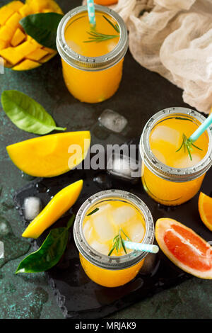 Cócteles de verano refrescante de cítricos y mango, bebida fría o una bebida con hielo sobre un fondo de piedra oscura.