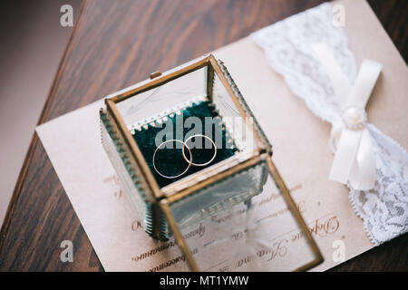 Hermosos anillos de boda de oro dentro de una caja de cristal vintage, sobre la invitación a la boda y de fondo de la tabla de madera Foto de stock