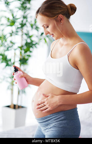 Las mujeres jóvenes embarazadas aplicar crema humectante en su vientre