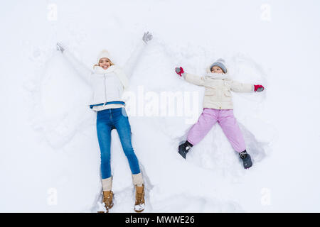 Vista superior de la feliz madre e hija haciendo ángeles de nieve juntos Foto de stock