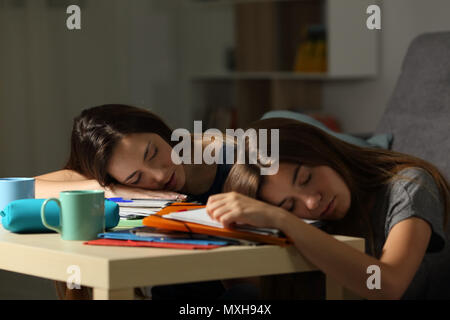 Dos estudiantes cansados durmiendo sobre notebooks después de horas estudiando hasta tarde en la noche en su domicilio. Foto de stock
