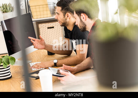 Borroso de cerca de una planta con compañeros sonriente y sentado delante de un ordenador en el fondo Foto de stock