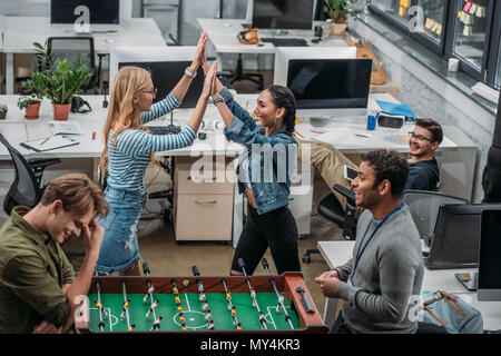 Colegas celebrando la victoria en el fútbol de mesa en la oficina moderna