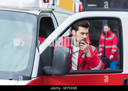 Hermoso macho paramédico hablando por radio portátil y de pie de la ambulancia Fotografía de - Alamy