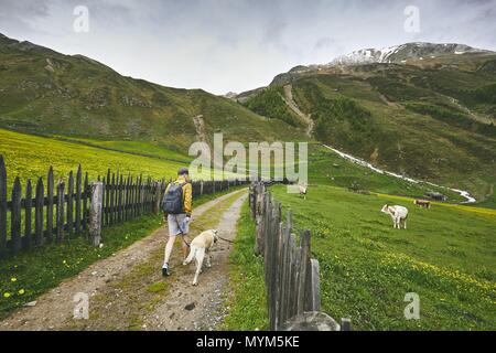 Turista con perro en campo. Joven caminando con el labrador retriever en camino de tierra. El Tirol del Sur, Italia