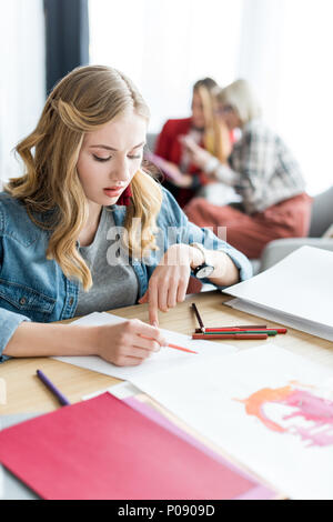 Joven rubia editor de la revista Bocetos de dibujo en la oficina moderna, colegas sentados detrás Foto de stock