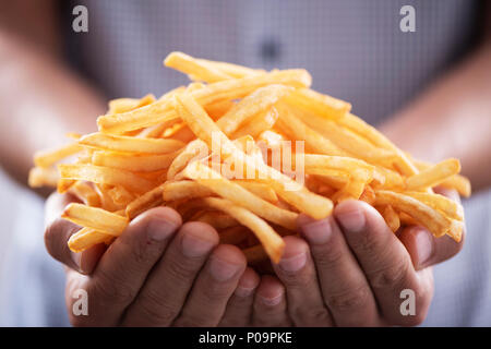 Primer plano de un joven hombre caucásico con un montón de apetitosas papas fritas en sus manos Foto de stock