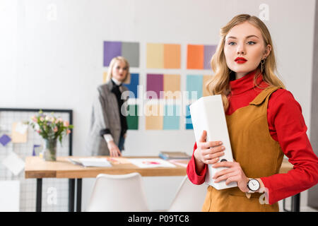 Editor de la revista de moda con carpeta en la oficina moderna con su colega y la paleta de colores en la pared detrás de Foto de stock