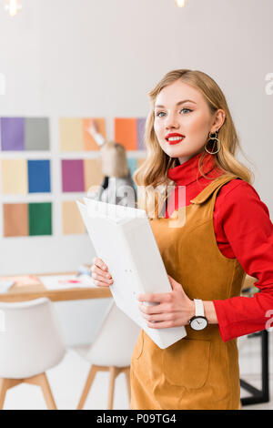 Editor de la revista atractiva con carpeta en la oficina moderna con su colega y la paleta de colores en la pared detrás de Foto de stock