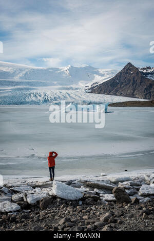 El hombre permanece congelada en la laguna con témpanos, montañas, laguna glaciar Fjallsárlón, al sur de Islandia, Islandia