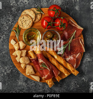 Selección de aperitivos de carne y queso. Jamón, queso parmesano, palos de pan, aceitunas, tomates en placa de madera, vista desde arriba. Foto de stock
