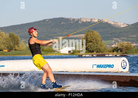 PASOHLAVKY, REPÚBLICA CHECA - Junio 03, 2017: Rider wakeboard en el cable wake park Merkur en Moravia del Sur, con las montañas al fondo Pálava Foto de stock