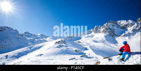 Feliz joven esquiador sentado en la cima de las montañas y disfrutando de la vista de los Alpes, Rhaetian Tonale pass, de Italia, de Europa. Foto de stock