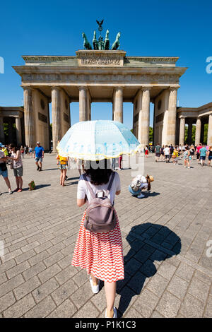 Turista chino con sun sombrilla delante de la Puerta de Brandenburgo en Berlín, Alemania