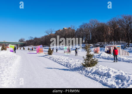 Las personas que caminan y patinar a lo largo del Río Rojo Sendero mutua en Winnipeg, donde el calentamiento artístico cabañas se encuentran en la pantalla; en Winnipeg, Manitoba, Canadá