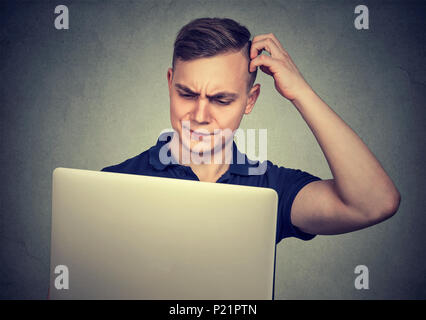 Joven hombre casual mirando perplejos mientras usa el portátil tiene dificultades con el dispositivo. Foto de stock