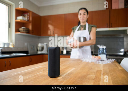 Mujer en su cocina mirando su altavoz inteligente Foto de stock